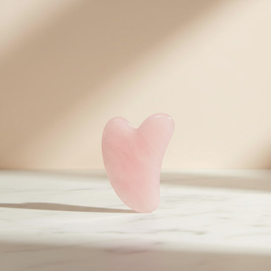 Arya Lush heart-shaped rose quartz gua sha tool for facial massage and skin firming on a marble surface.